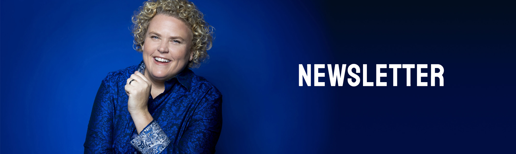 Comedian Fortune Feimster in front of a vivid blue background wearing a blue paisley shirt.