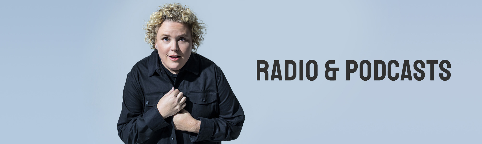 Comedian Fortune Feimster wearing a dark jacket in front of a pale blue background.