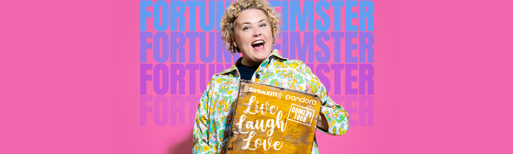 Comedian Fortune Feimster holding a wooden sign showing the words Live Laugh Love Comedy Tour on SiriusXM and Pandora.
